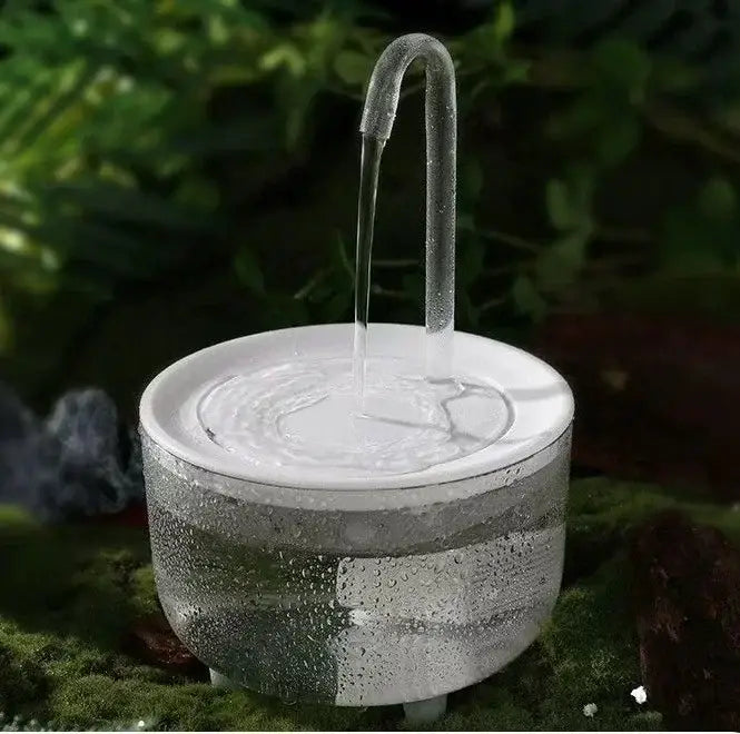 klarer Glas-Automatik-Trinkwasserspender für Haustiere mit gebogenem Auslauf, der Wasser in eine weiße Keramikschale abgibt, von vorne betrachtet