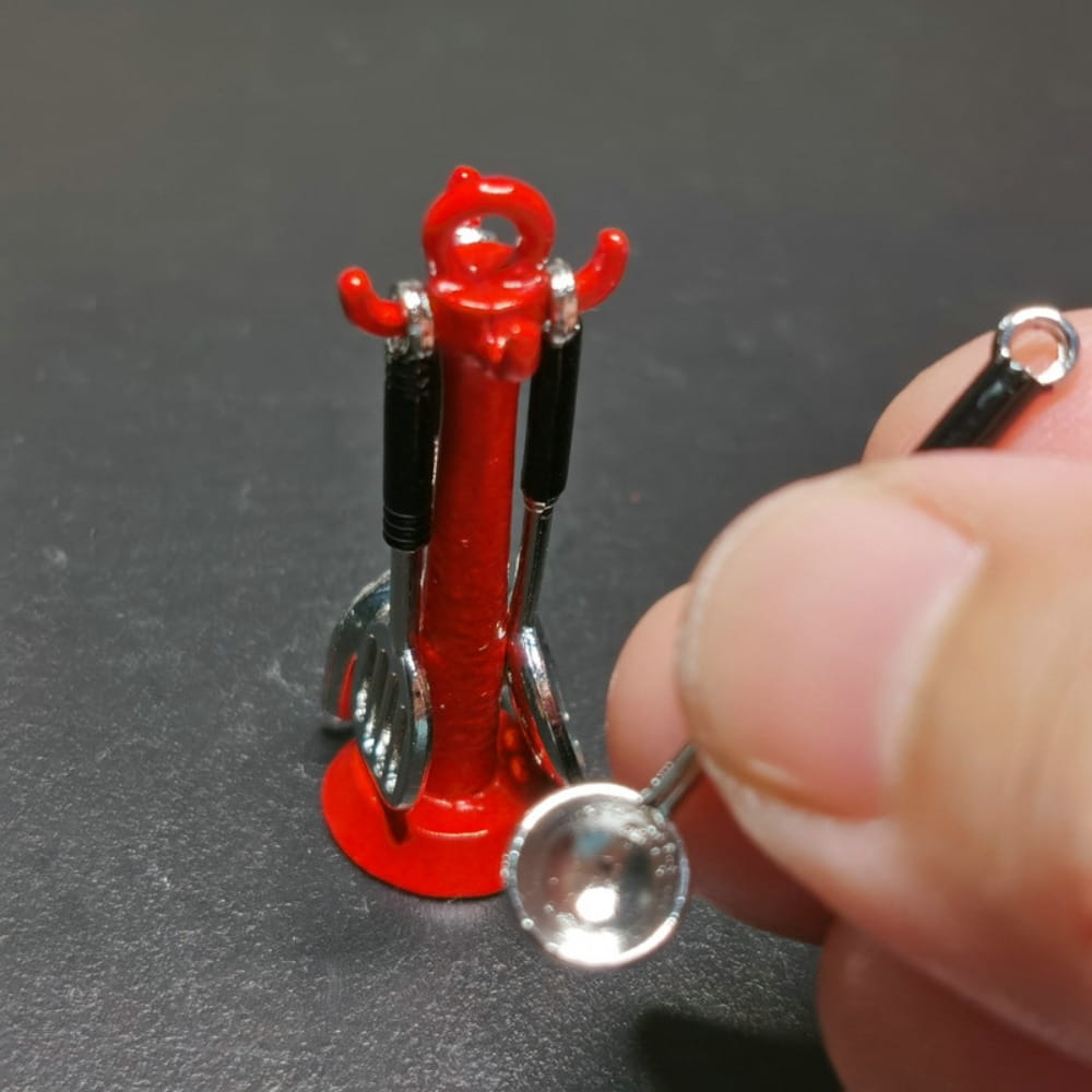 Support d’ustensiles de cuisine miniature rouge avec poignées noires et argentées, tenant de petites cuillères et louches dans un ensemble d’ustensiles de cuisine miniature pour maison de poupée.