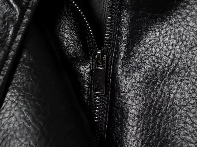 金属のプルタブを付けた、黒のレザージャケットのジッパーのクローズアップを特徴とする黒のフェイクレザーボンバージャケット。