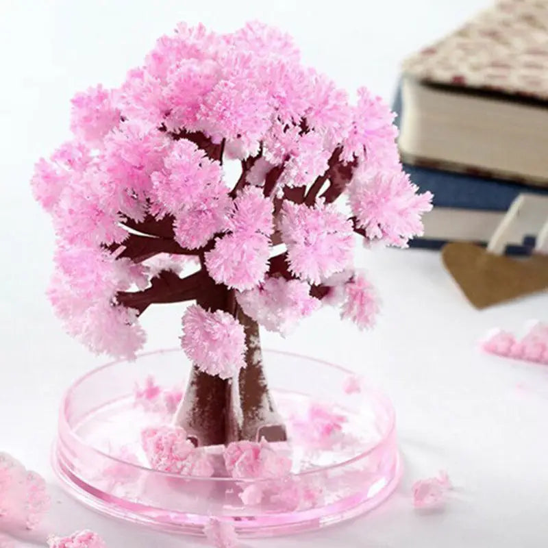 A pink crystalline cherry blossom magic growing Christmas tree with a brown trunk displayed in a clear circular base as a tabletop toy.