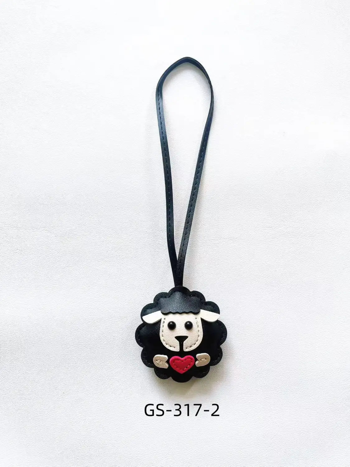 Leather sheep keychain made of black leather with a white face red heart and gold accents serving as a cute animal bag charm.