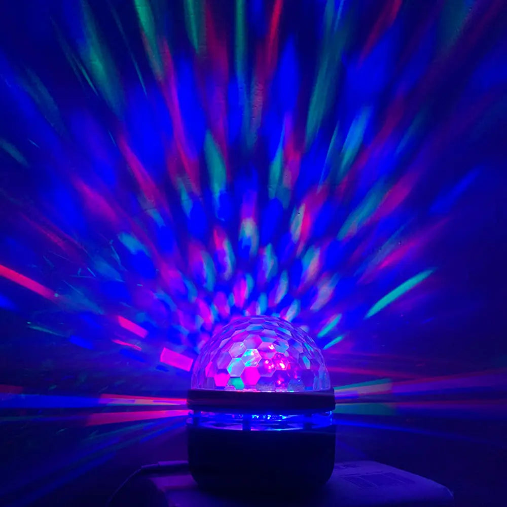Une veilleuse de projection de ciel étoilé comprenant une boule disco lumineuse avec une coupole transparente facettée, émettant des faisceaux bleus et pourpres vibrants.