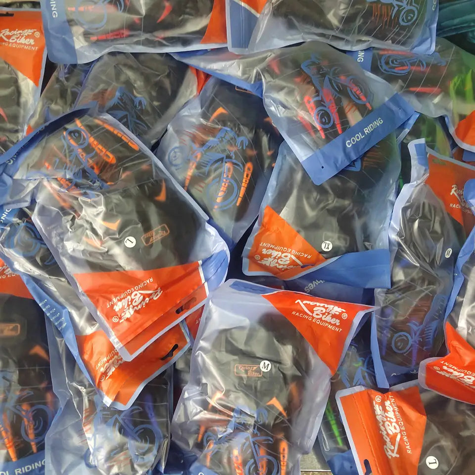 Black and orange breathable motorcycle racing gloves in clear plastic packaging with blue accents for protective gear use.