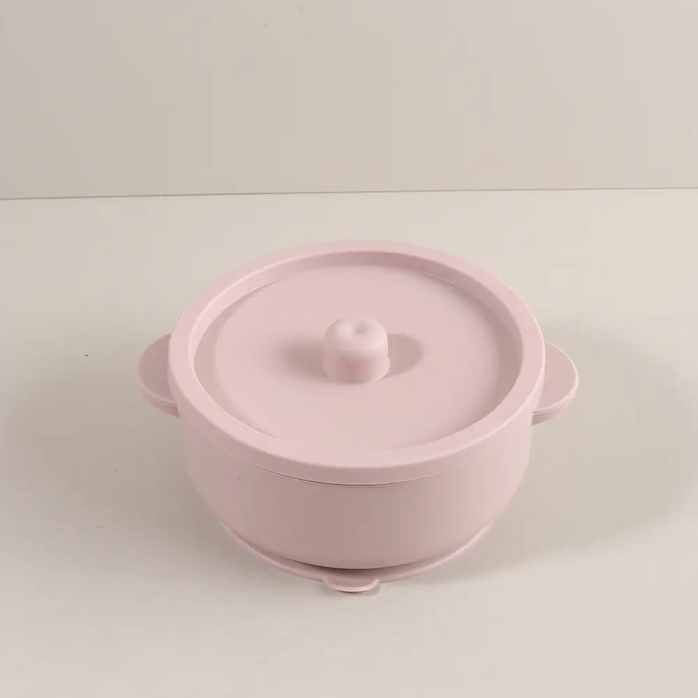 Rosa Silikon-Baby-Trainingsschüssel mit abgerundeten Griffen und passendem Deckel mit kleinem Knopf, zur Verwendung für das Zufüttern und die Zufuhr von Speisen.