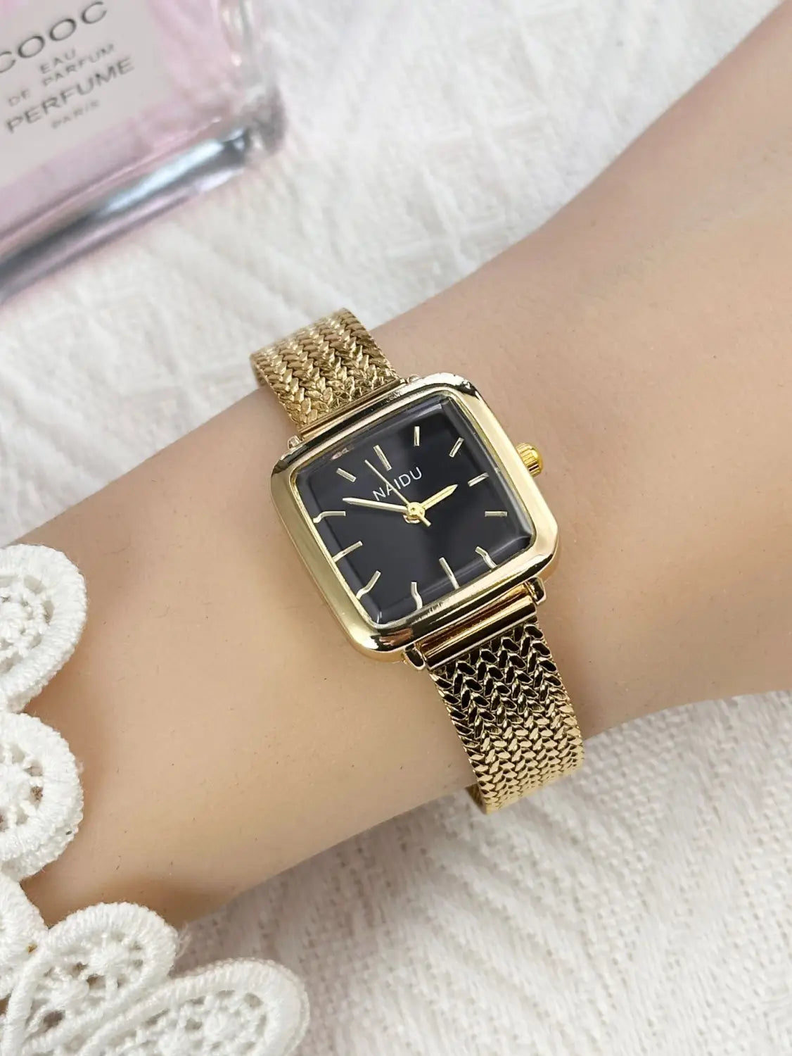 Minimalist square quartz watch for women featuring a gold-toned mesh bracelet and a black dial with minimalist gold hands.
