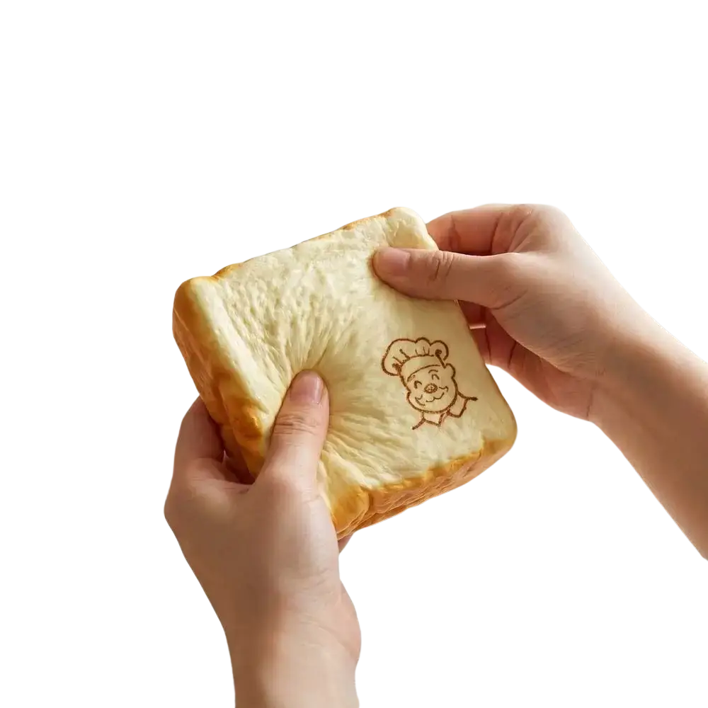 A soft bread-shaped fidget toy with a golden-brown crust and embroidered chef design recommend age universal age range