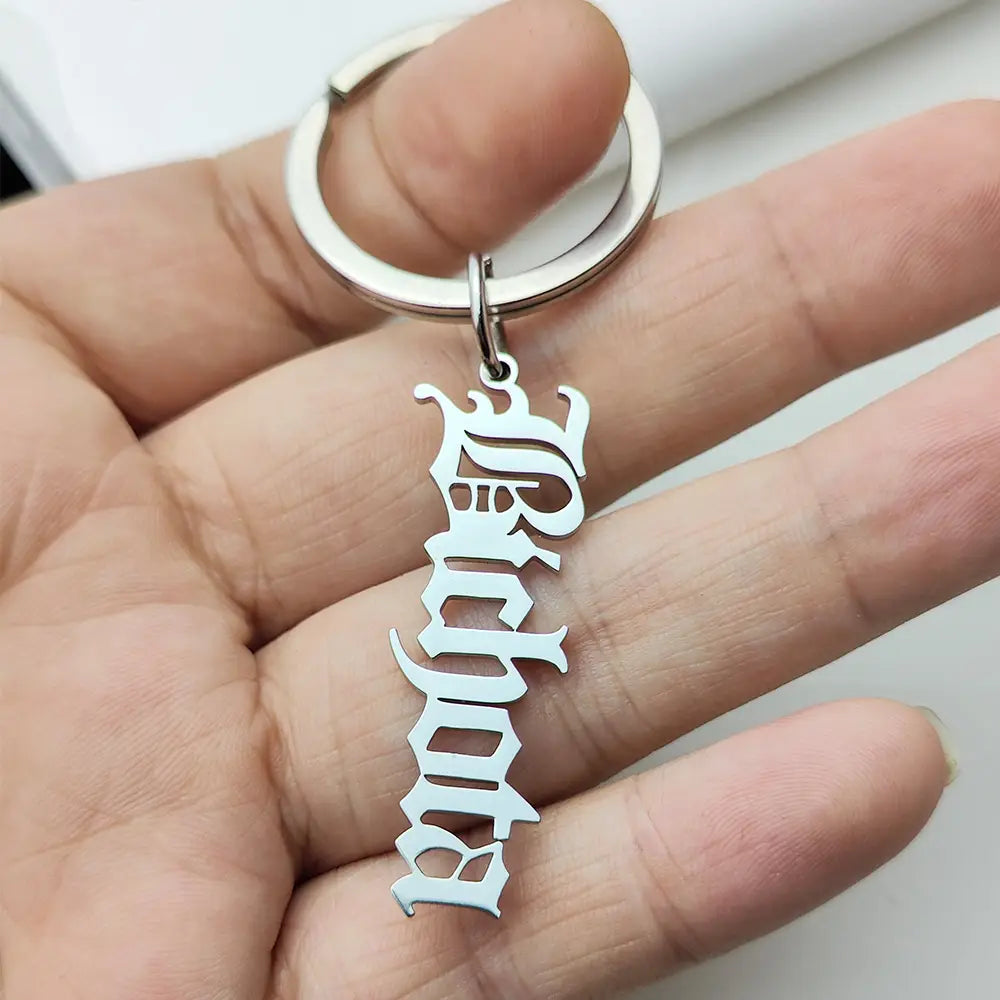 Llavero de nombre personalizado de metal plateado, hecho de joyería de acero inoxidable, con un dije de estilo gótico ornamental con letras orientadas verticalmente.