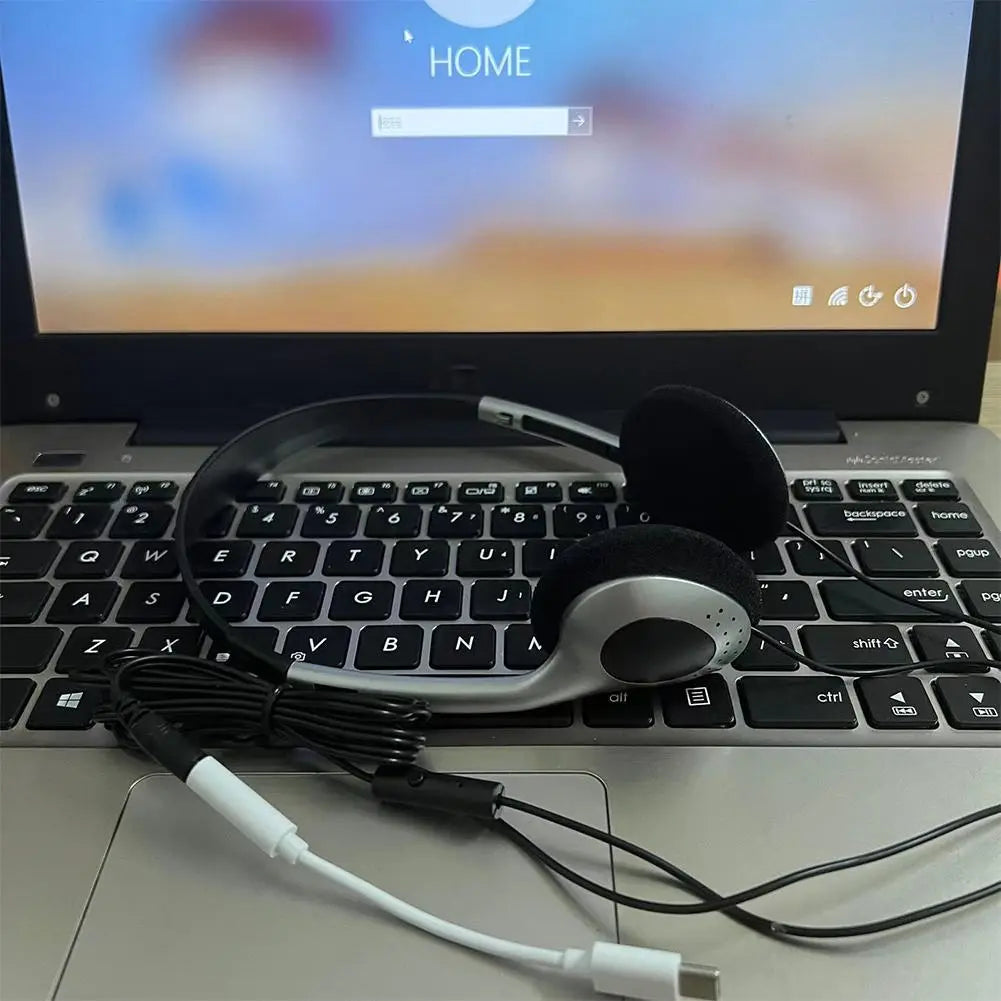 Casque d’écoute supra-auriculaire rétro filaire argent et noir avec câble spiralé, posé sur le clavier d’un ordinateur portable.