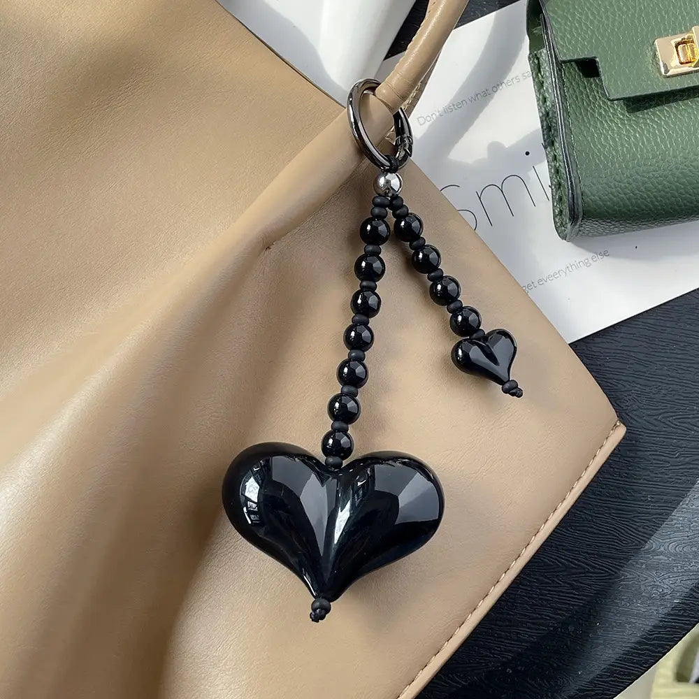 Porte-clés pour sac en forme de cœur brillant noir avec chaîne à perles et petit accent en forme de cœur, destiné à l’accessoirisation du sac.