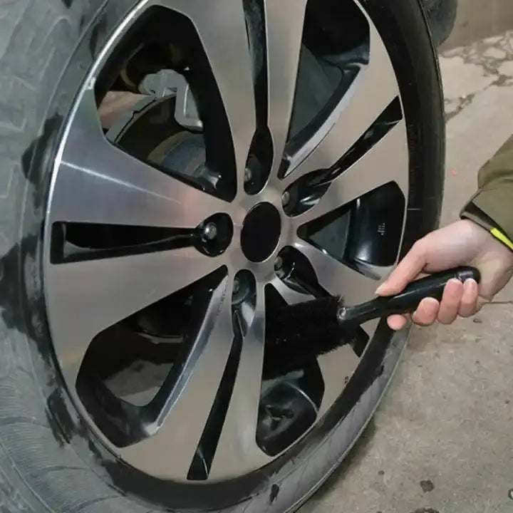 Brosse de nettoyage pour roues de voiture en microfibre à poignée noire, utilisée pour nettoyer une jante en alliage argentée brillante.