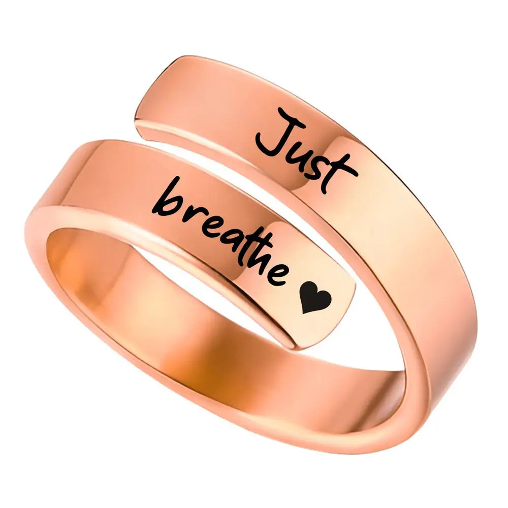 A rose gold stainless steel wrap-around anxiety ring engraved with just breathe in black script and a small heart symbol.