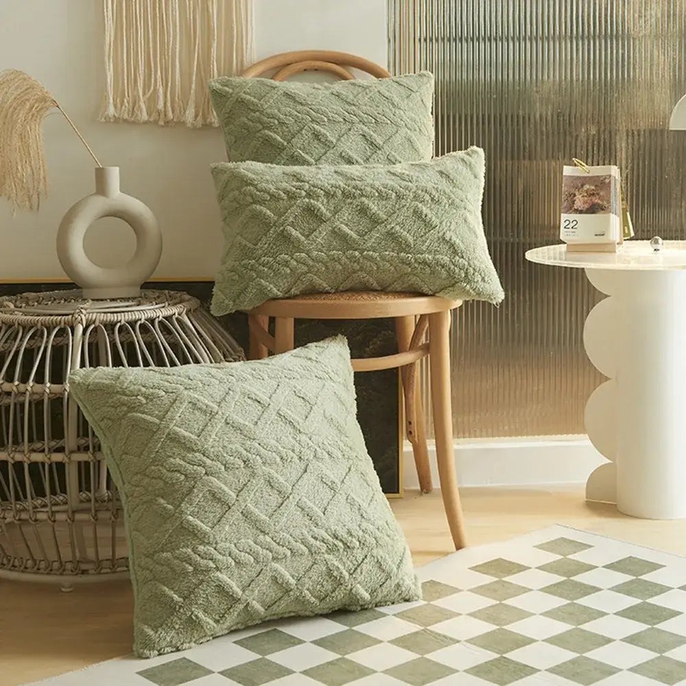 Three sage green plush geometric throw pillow covers 45x45cm with a textured diamond-patterned knit design arranged on and around a wooden chair.