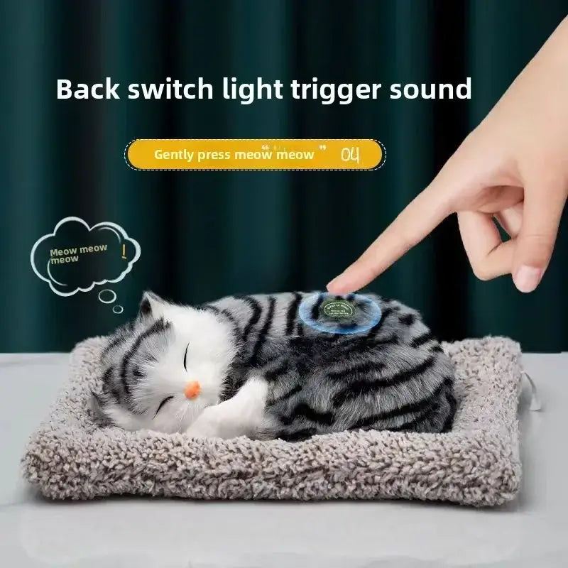 A plush gray and white tabby cat toy with black stripes lies on a soft textured bed, designed as a simulated sleeping cat plush toy with sound.