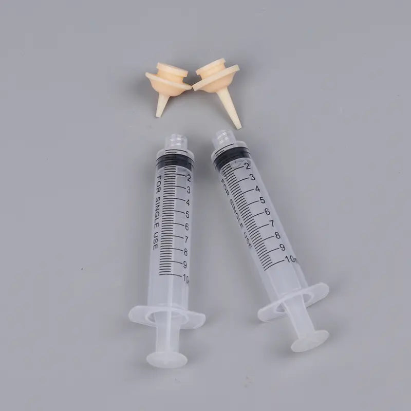 Two transparent plastic oral syringes with black measurement markings and white plunger caps in 1ml 3ml 5ml sizes accompanied by beige silicone nipple feeders for pet use
