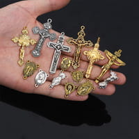 A hand holds a collection of gold and silver-toned religious cross pendants showcasing intricate detailing next to a Saint Christopher leather keychain in antique bronze.