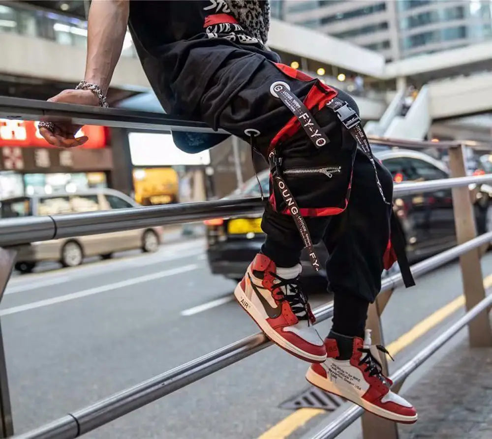 Pantalon cargo joggers streetwear pour hommes en noir et rouge, avec marquage blanc et poches zippées, conçu pour une tenue décontractée.