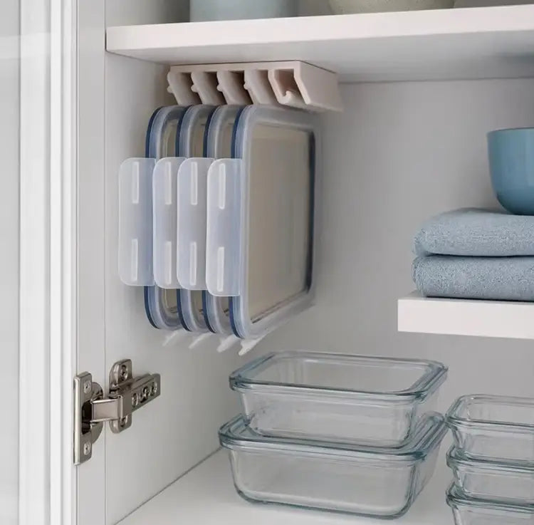 Porte-couvercles de rangement en plastique blanc, contenant quatre boîtes alimentaires à couvercles translucides bleus, conçues pour un rangement peu encombrant et organisé des couvercles.