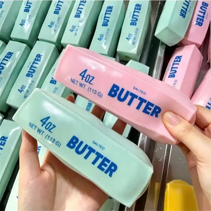Rosa- und mintgrüne gesalzene Butterriegel mit der Aufschrift 4oz Butter in kräftiger blauer Beschriftung, als Butterstick-ASMR-Sensory-Squishy-Spielzeuge dargestellt.