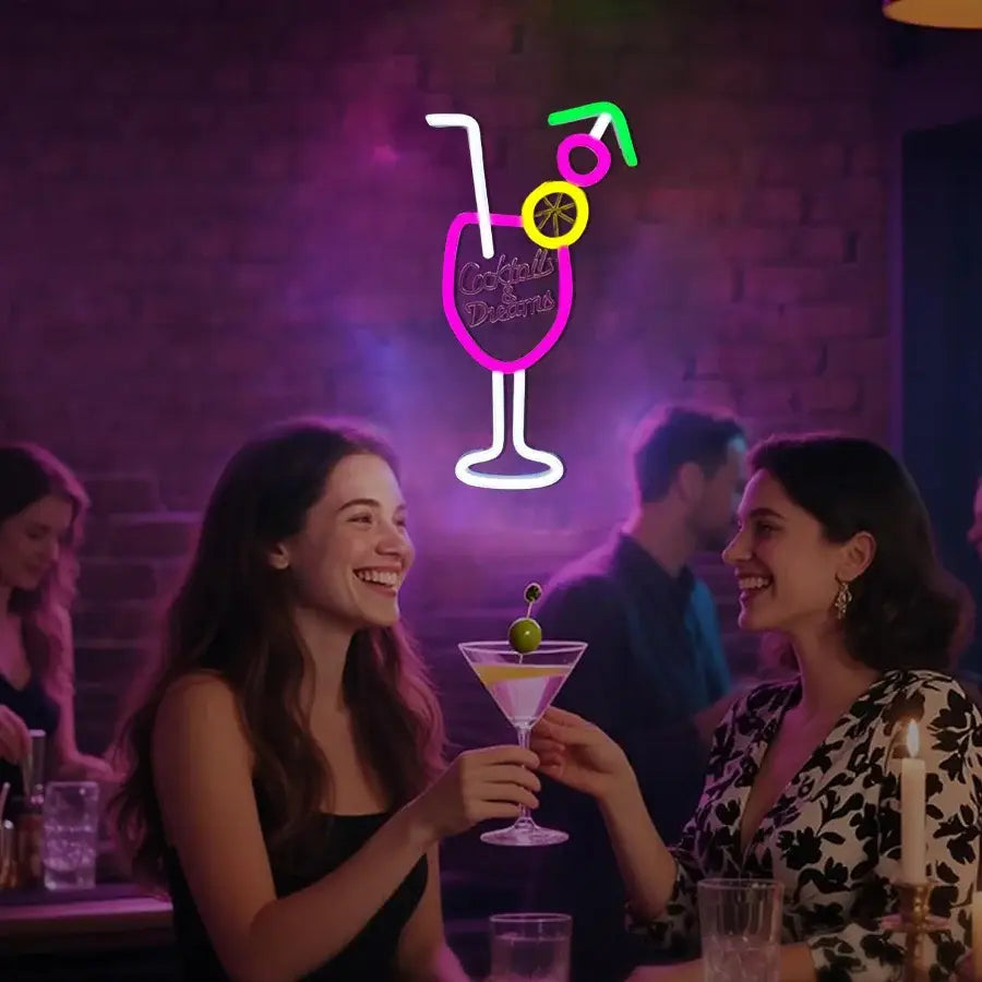 un enseigne néon vibrante d’un verre à cocktail avec un bord rose, une tige et une base blanches, une tranche de citron jaune, une cerise verte, et une paille multicolore dans le design de l’enseigne néon « Cocktails and Dreams »