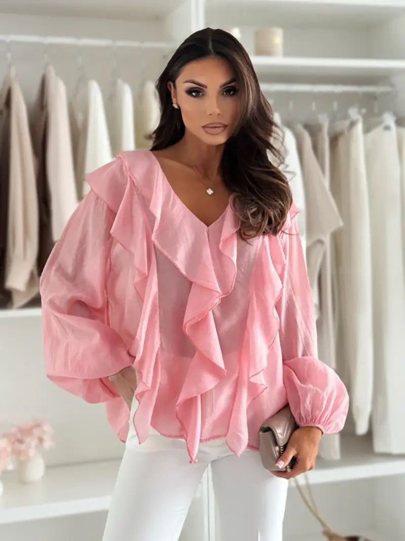 Une blouse transparente rose pâle, ornée de volants superposés et de manches bouffantes, avec un design blanc à encolure en V à volants.