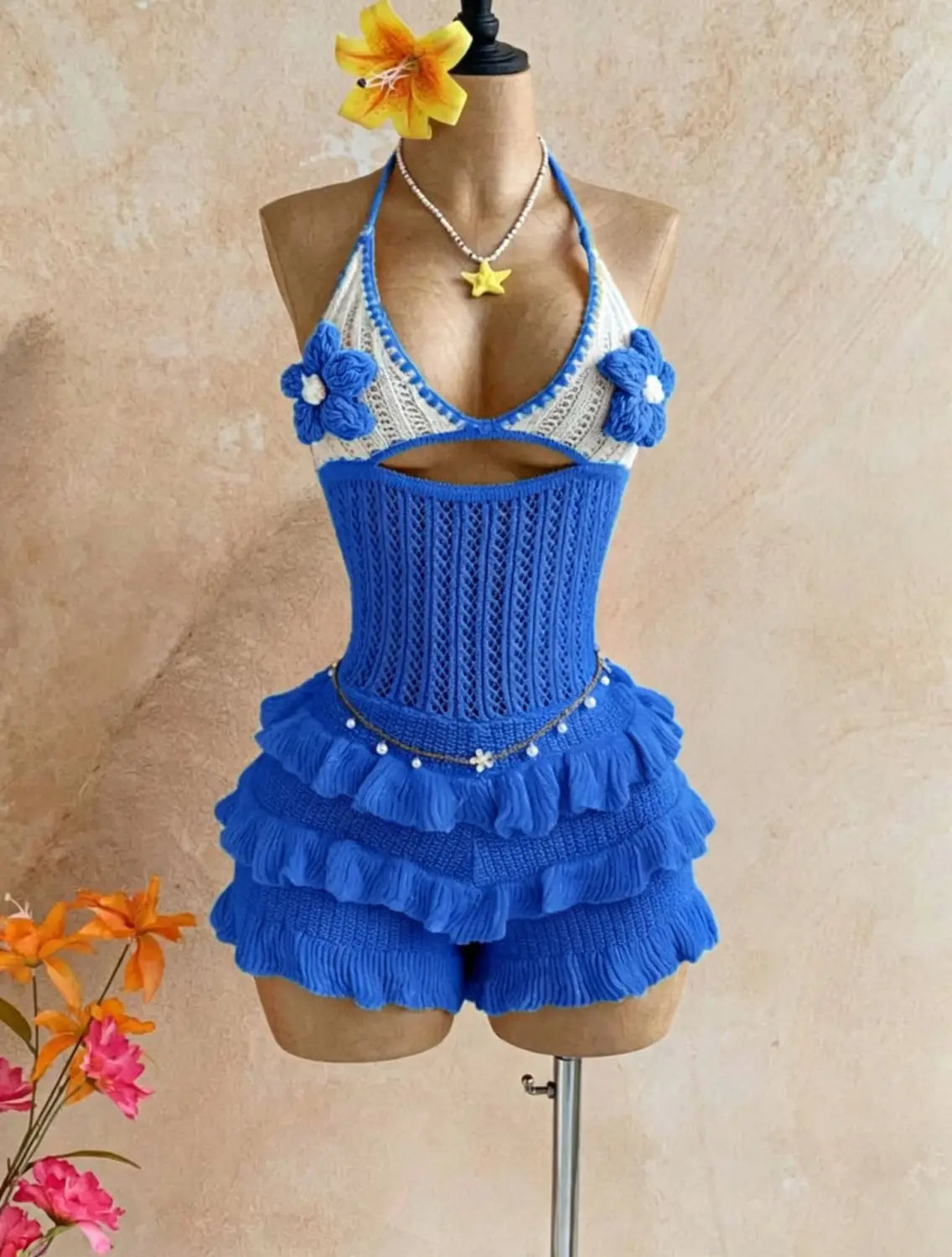 A vibrant blue and white crocheted knitted ruffle halter romper summer playsuit with floral embellishments and ruffled shorts paired with a star necklace.