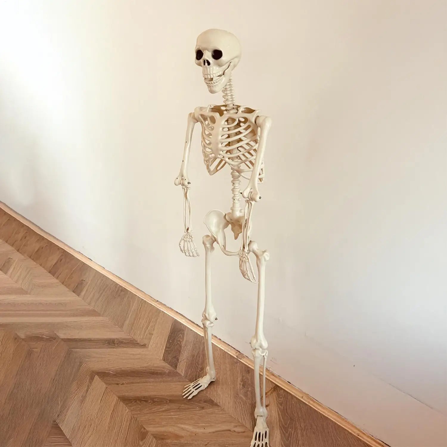 una figura de esqueleto de plástico color marfil pálido de tamaño completo para Halloween, de pie y erguida, como decoración posable para jardín en un ambiente de casa encantada