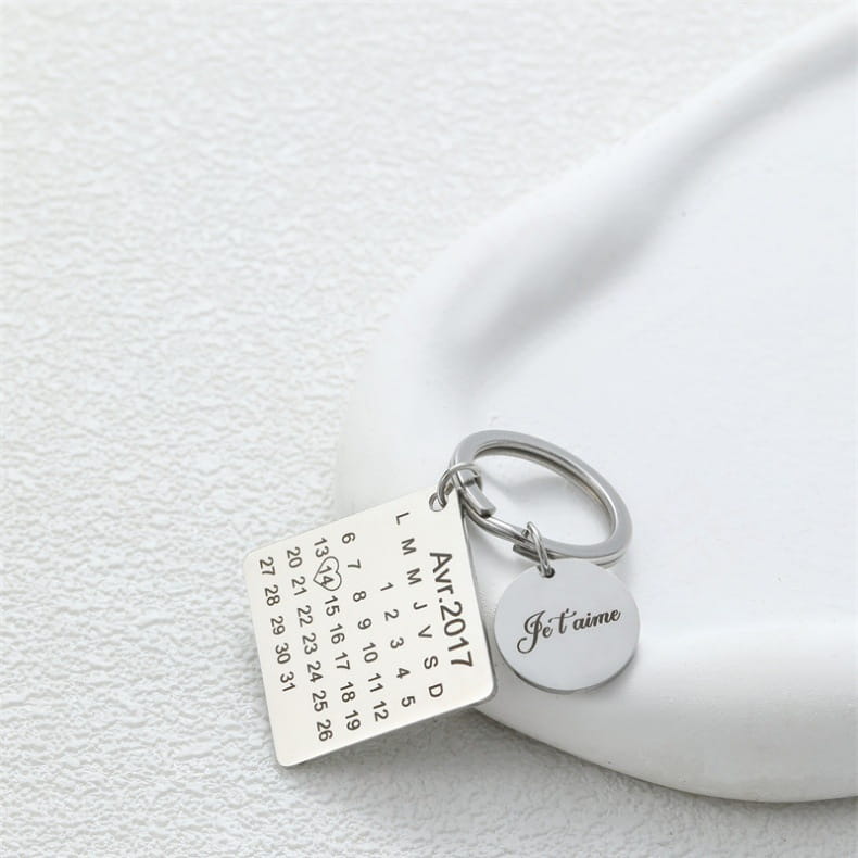 silver keychain featuring a rectangular calendar charm engraved with dates and months and a circular disc inscribed with je taime for a personalized anniversary gift