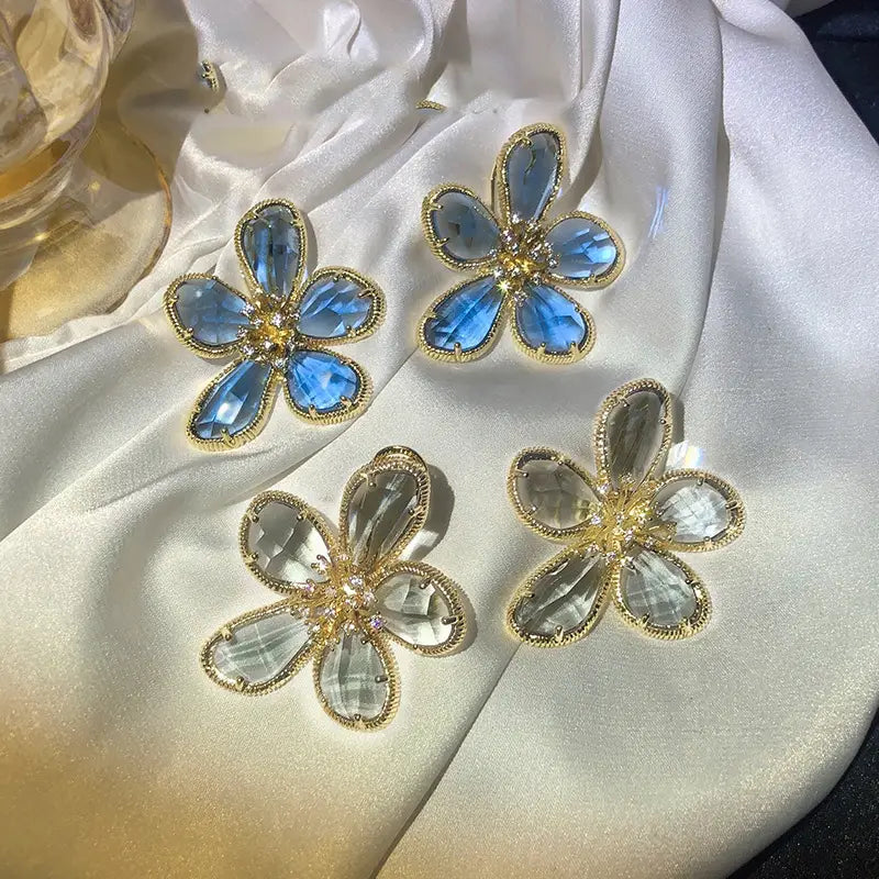 金色調の金属フレームに、ファセットカットの青色クリスタルと透明クリスタルをあしらった、花の形のエレガントなデザインのゴールドフラワークリスタルスタッドピアス。