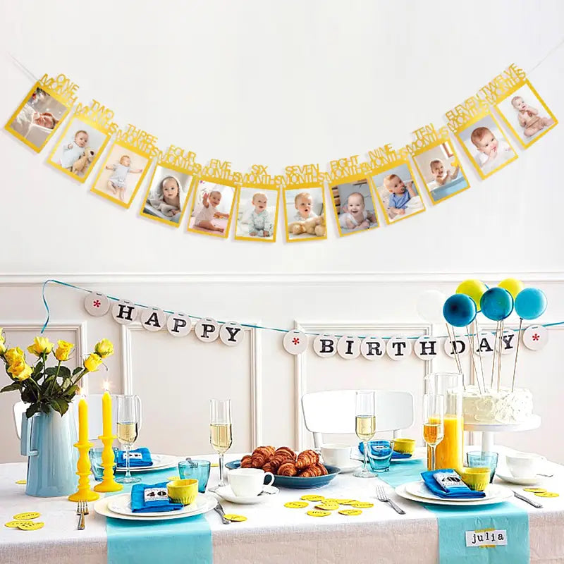 Yellow 1st birthday photo banner with numbers and baby photos hanging above a birthday table featuring a monthly picture garland.