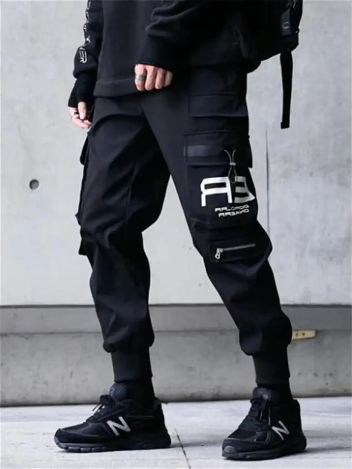 Pantalones tipo jogger cargo negros para hombres con múltiples bolsillos y un logotipo gráfico blanco en el muslo, diseñados para estilo urbano y uso casual.