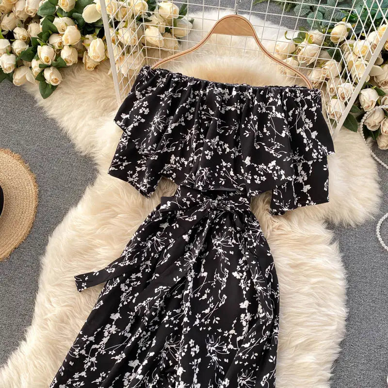 Enterizo de pierna ancha negro con estampado floral, escote tipo bardot, con estampado blanco y mangas con volante, exhibido en una percha de madera