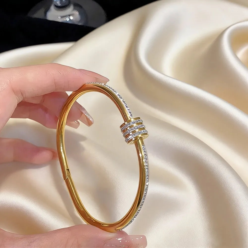 Stainless steel gold-toned bangle bracelet for women with a sleek modern design featuring embedded clear stones and a distinctive triple-layered clasp.