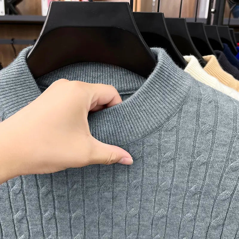 Ein grauer Zopfstrick-Pullover aus dickem Garn mit geripptem Rundhalsausschnitt, dargestellt auf einem schwarzen Kleiderbügel in der Produktlinie Herren-Zopfstrick-Pullover mit Rundhalsausschnitt.