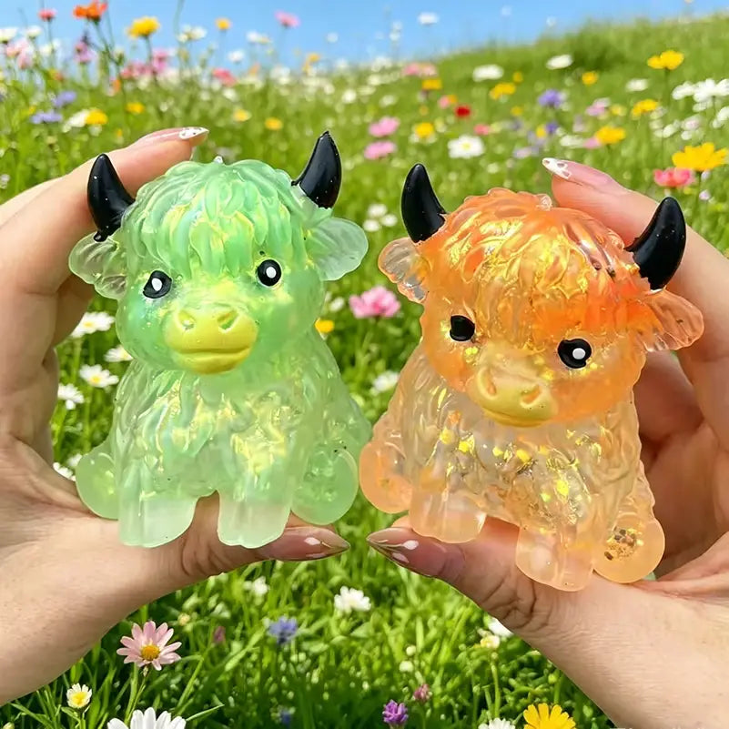 Two translucent, glitter-filled highland cow sensory fidget toys in vibrant green and warm orange with black horns and yellow snouts designed for stress relief.