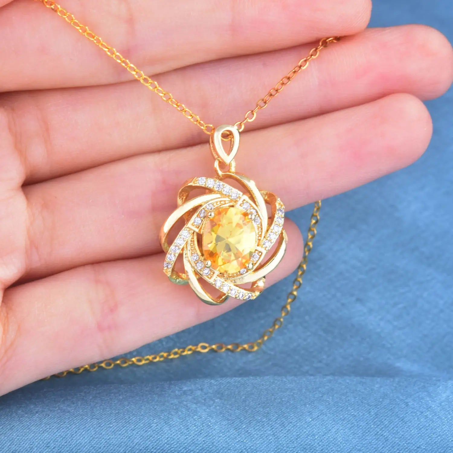 Collier pendentif moulin à vent en citrine doré en or comportant une pierre jaune centrale entourée de bandes métalliques tourbillonnantes et de petites pierres transparentes.