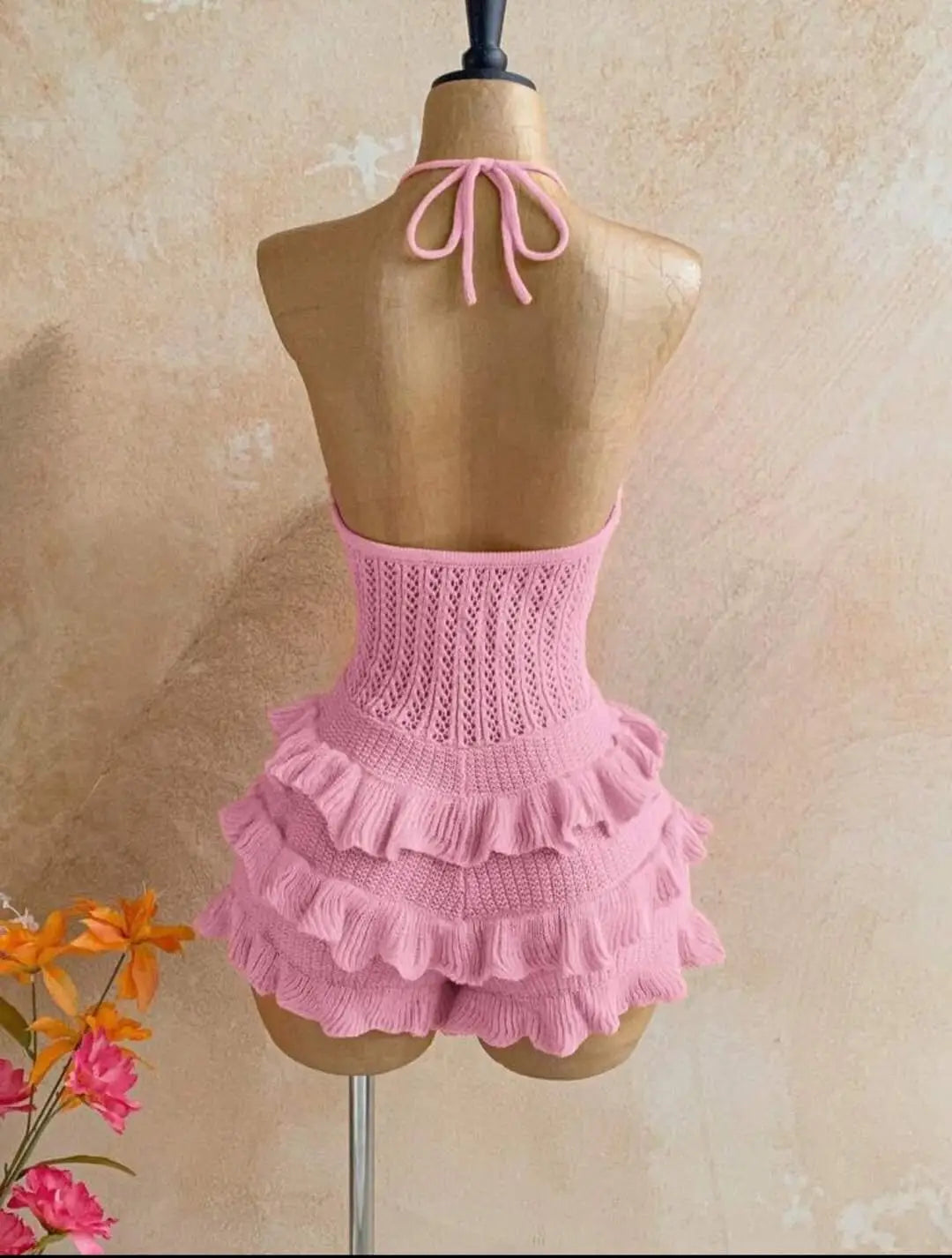A delicate pink knitted ruffle halter romper summer playsuit with tiered ruffles and a tied back detail shown from the back side.