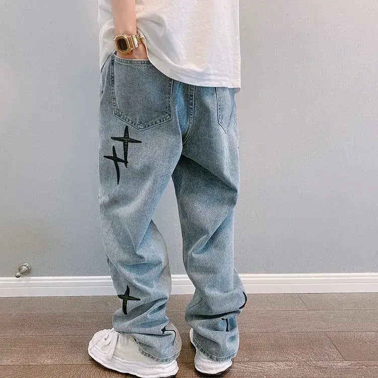 Jeans en denim délavé clair ample à jambes larges à broderie croisée, avec broderie croisée noire sur la cuisse externe et la partie inférieure de la jambe, coupe décontractée et revers retroussés.