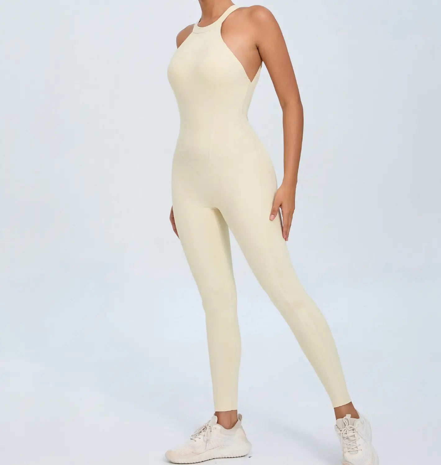 Cream-colored form-fitting seamless one-piece athletic jumpsuit with a halter neckline designed for workouts shown from the back.
