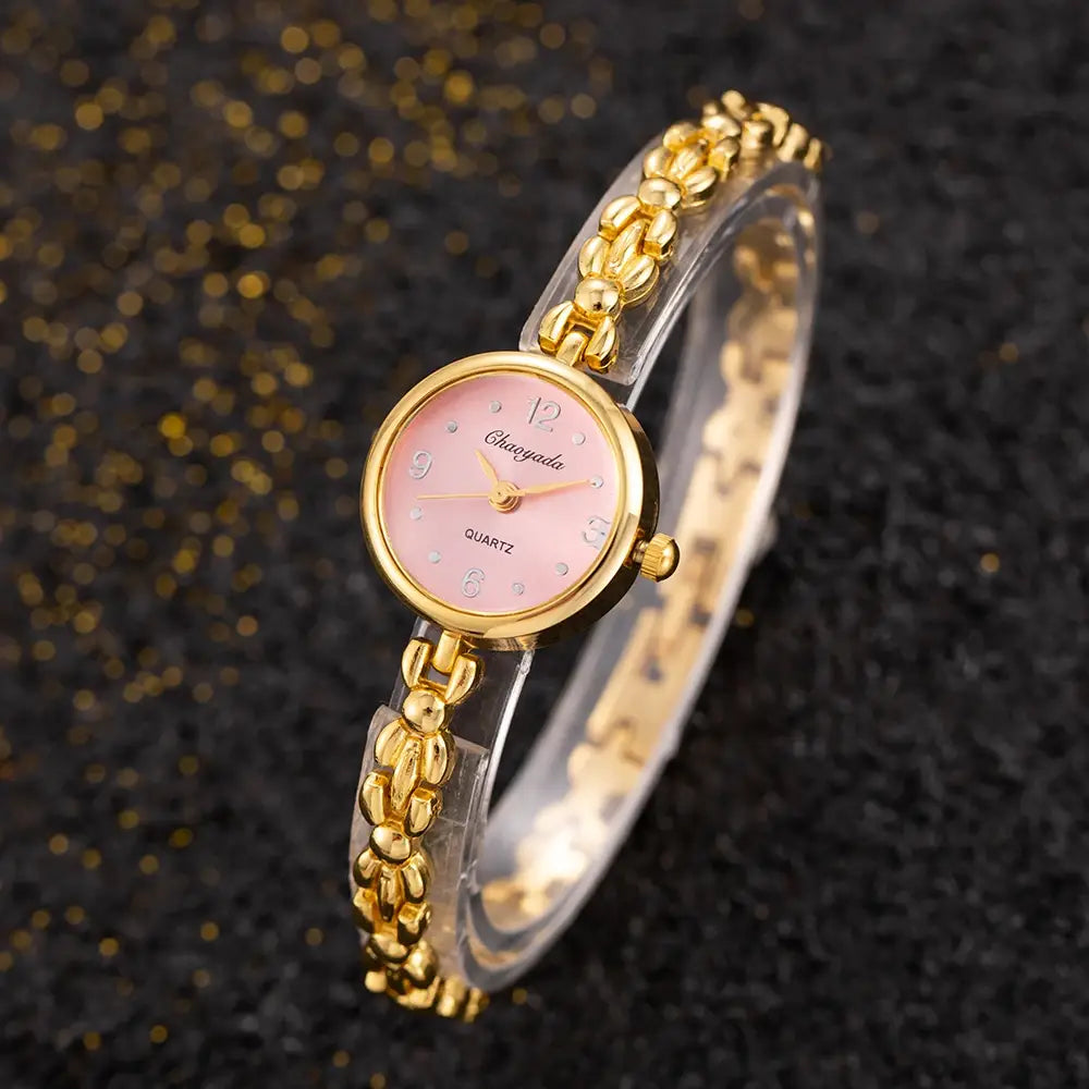 Gold ladies bracelet watch small dial quartz wristwatch with a gold-toned case, pink dial, and clear plastic links