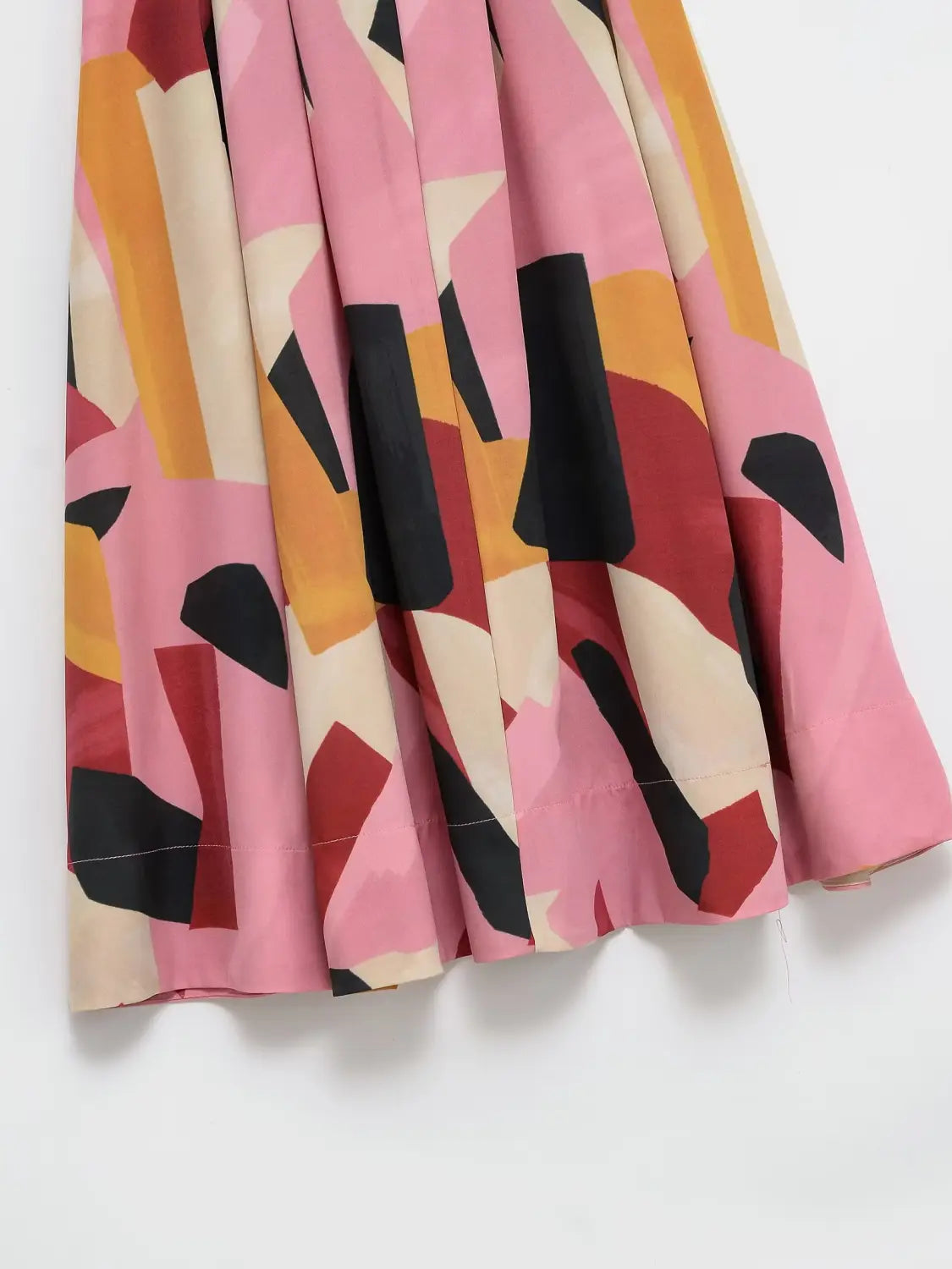 Ein plissierter geometrischer Satin-Midirock mit einem kräftigen abstrakten Muster in Schattierungen von Rosa, Orange, Schwarz und Creme.