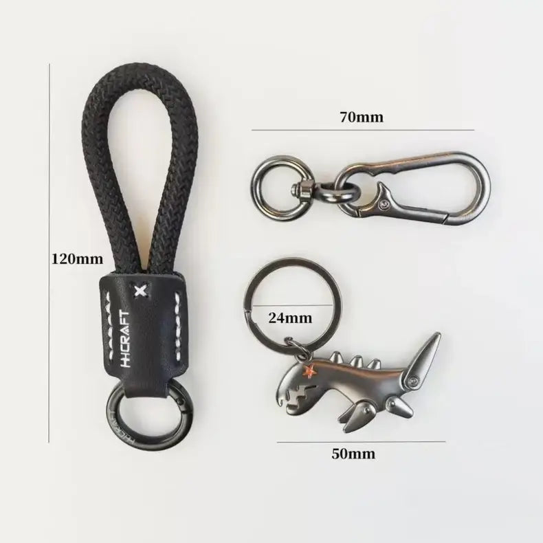 Black leather dinosaur keychain with braided cord and metallic shark-shaped charm for bag pendant.