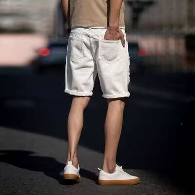 Les shorts en jean blanc déchiré dans un style streetwear décontracté, avec des revers roulés et un aspect légèrement usé.