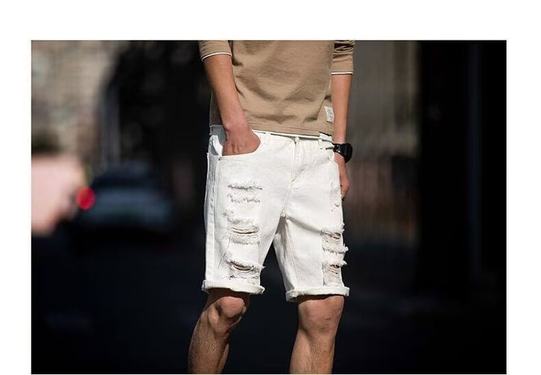 Les shorts en jean blanc déchiré comportent des détails vieillis et des revers roulés pour un style streetwear.
