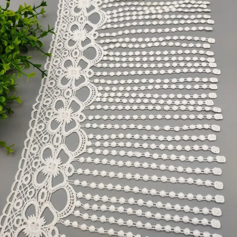 Tissu à bordure de dentelle à perles blanches, présentant une bordure de dentelle blanche avec des motifs floraux délicats et un frange de perles.