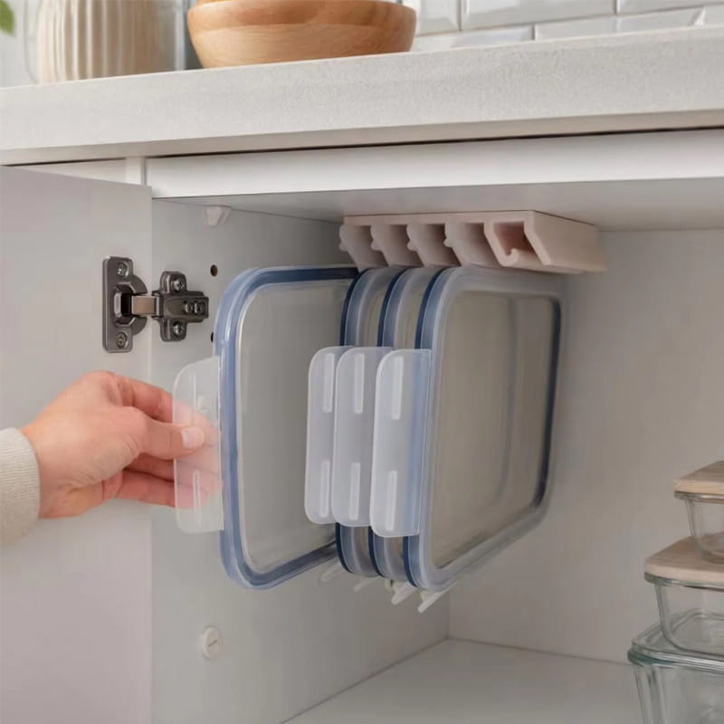 Récipients de conservation des aliments en plastique transparent, avec couvercles à bord bleu, rangés avec soin et suspendus à un support de couvercles de récipients de conservation des aliments en plastique beige et à une tringle sous étagère fixée à un organisateur de placard.