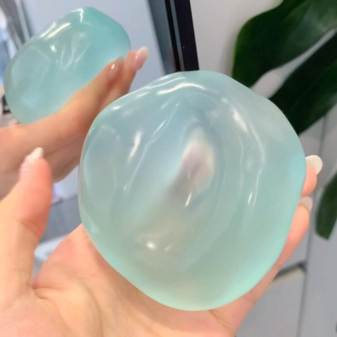 eine durchscheinende hellblaue Gel-ähnliche Stresskugel, die in der Hand gehalten wird, dargestellt als blaues Kokosöl-Quetschspielzeug.