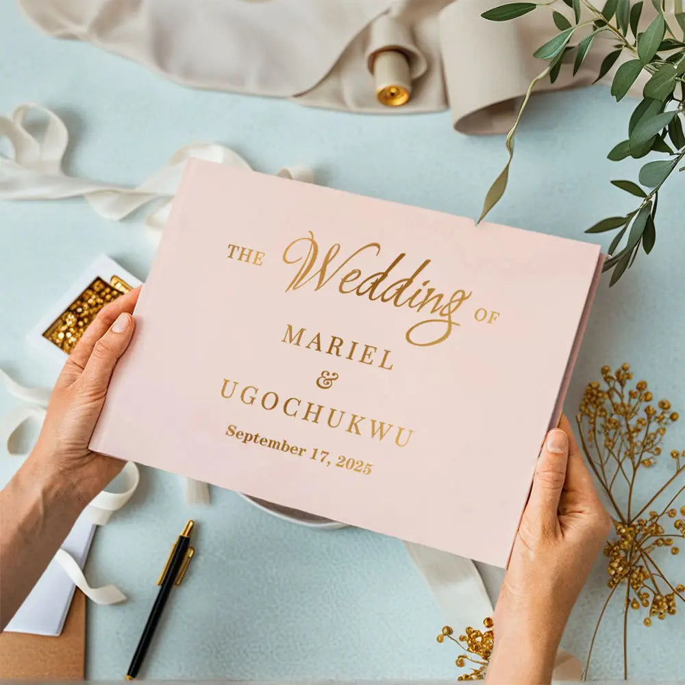 A soft pink personalized wedding guest book with elegant gold foil lettering and included pen for wedding use.