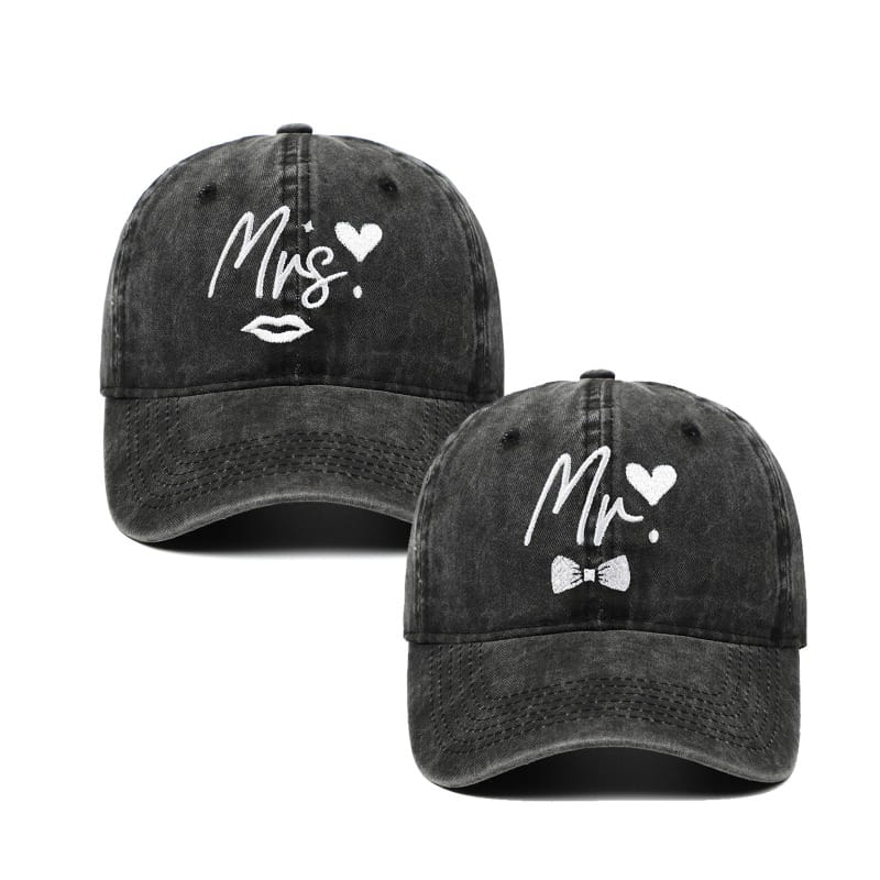 Une paire de casquettes de baseball noires délavées avec broderie représentant « MRS » et un cœur au-dessus de lèvres stylisées, ainsi que « MR » et un cœur au-dessus d’un nœud papillon, provenant de la collection de chapeaux parentales « Mr et Mrs » brodés.