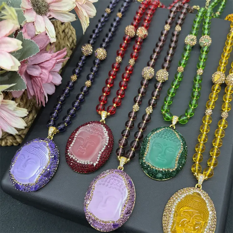 Un ensemble de cinq colliers de pendentifs Bouddha colorés, comportant des visages sculptés de forme ovale avec des halos ornés de strass sur des chaînes à perles aux teintes assorties, adaptés à divers âges applicables et dotés de fermetures à pince en forme de sésame.