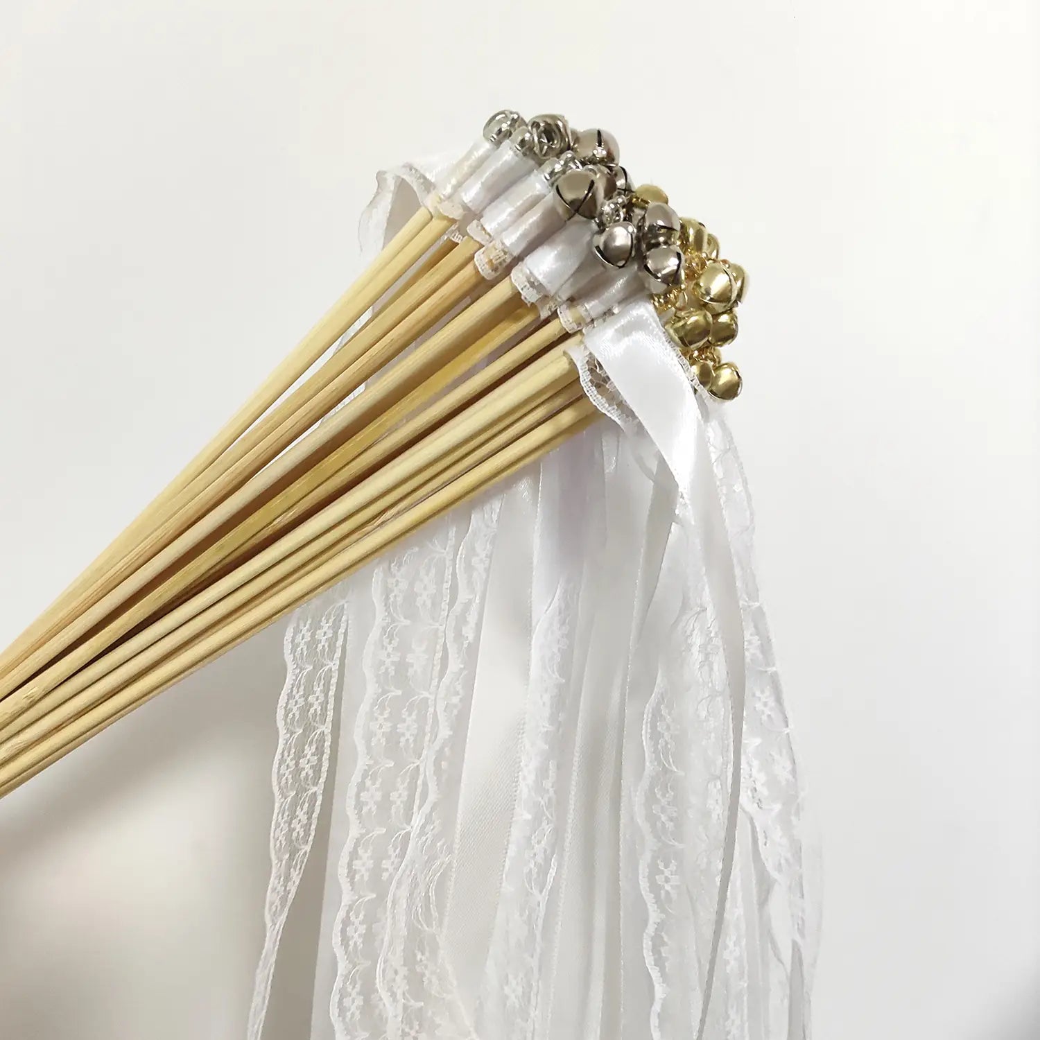 Un assortiment de baguettes de ruban de mariage en bois ornées de cloches argentées et dorées, enveloppées dans un tissu délicat en dentelle blanche.
